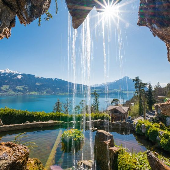 Kleiner Wasserfall tropft vor Felsguckloch, Sonne scheint, Panoramablick Richtung Berge und Thunersee