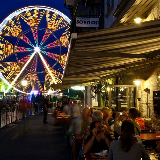 Thun bei Nacht am Aarequai mit Blick Richtung Mühleplatz und auf buntes, grosses Riesenrad.