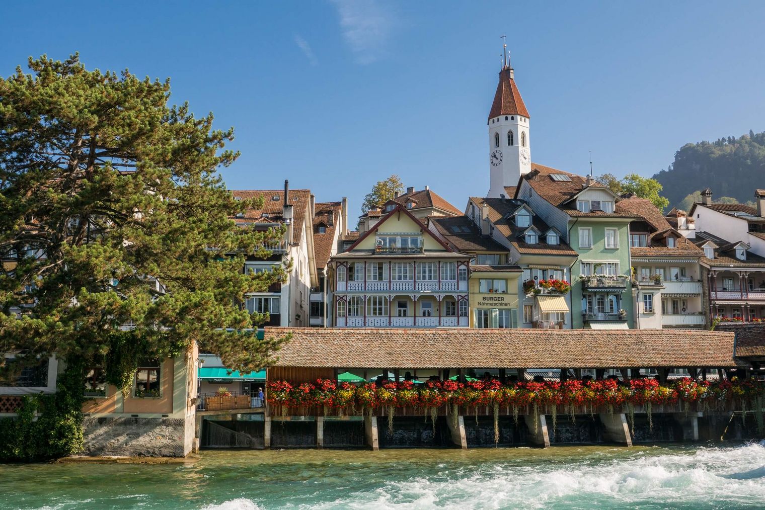 Eindrucksvolle Szenerie inmitten der Stadt Thun mit der sprudelnden Aare, die durch die untere Schleuse fliesst und Altstadt inklusive Kirche im Hintergrund.