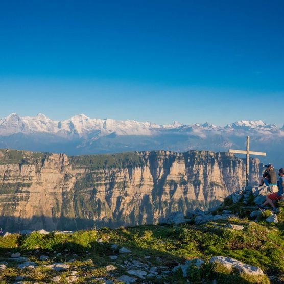 Drei Freunde bestaunen vom Gipfelkreuz des Sigriswiler Rothorn das Panorama