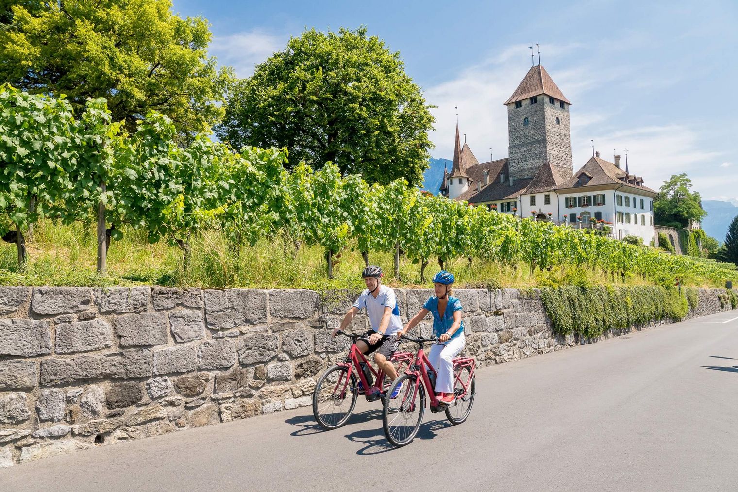 Ein Paar fährt mit gemieteten E-Bikes vorbei am Schloss Spiez und am Spiezer Rebberg