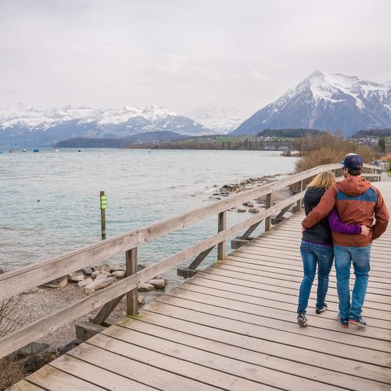 Ein junges Paar spaziert über den Holzsteg im Bonstettenpark und geniesst das Frühlingserwachen am Thunersee