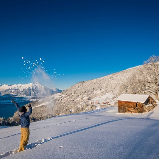 Mann wirft Schnee in die Luft in Beatenberg mit strahlend blauem Himmel